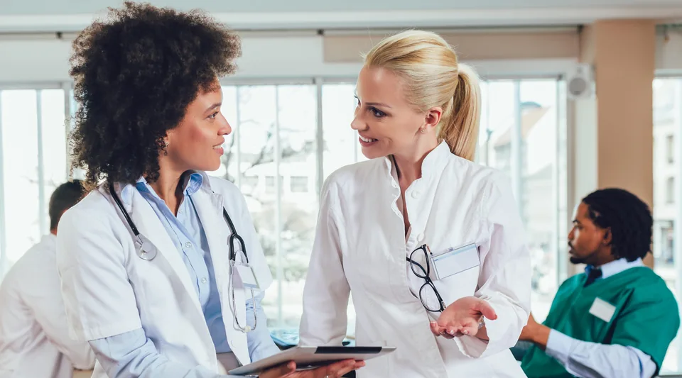 Two healthcare professionals discussing a tablet in a clinical workplace.
