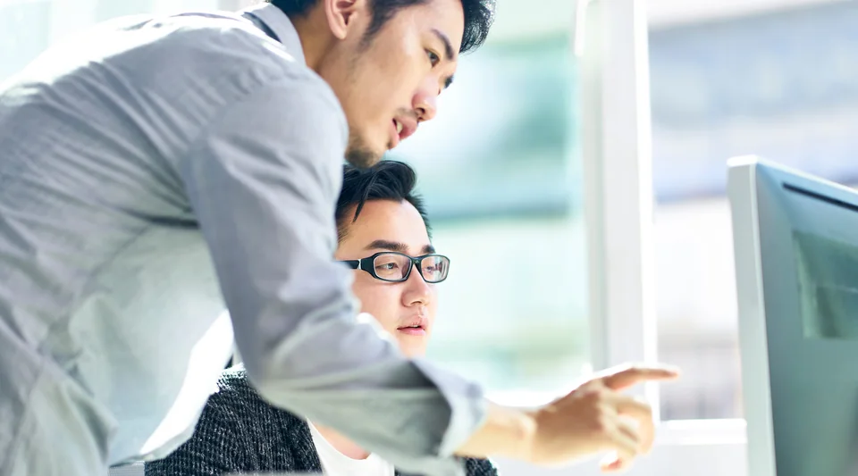 A colleague pointing something out on an office computer screen.
