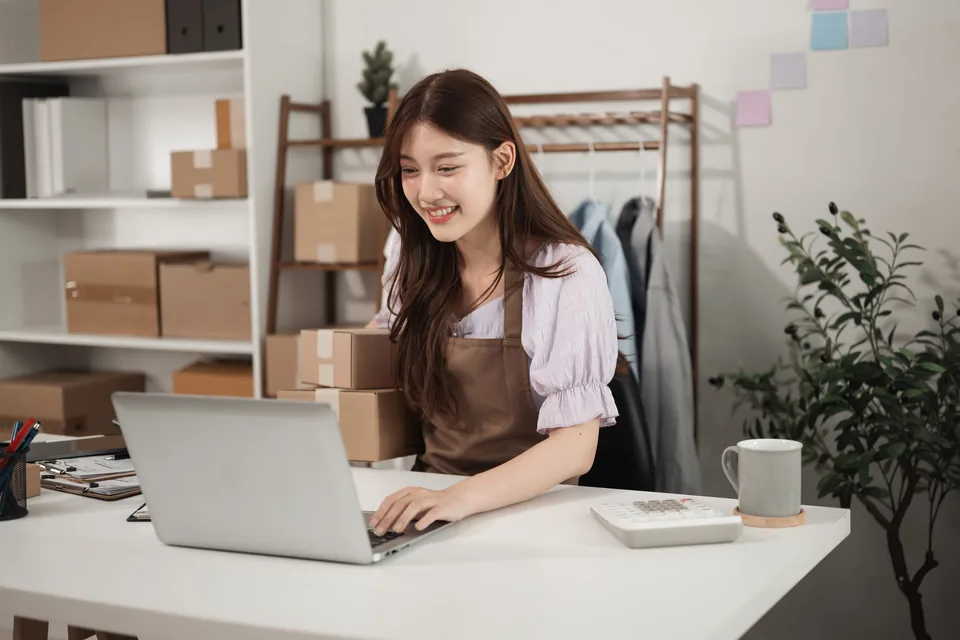 A clothing retailer using a laptop beside packed orders.