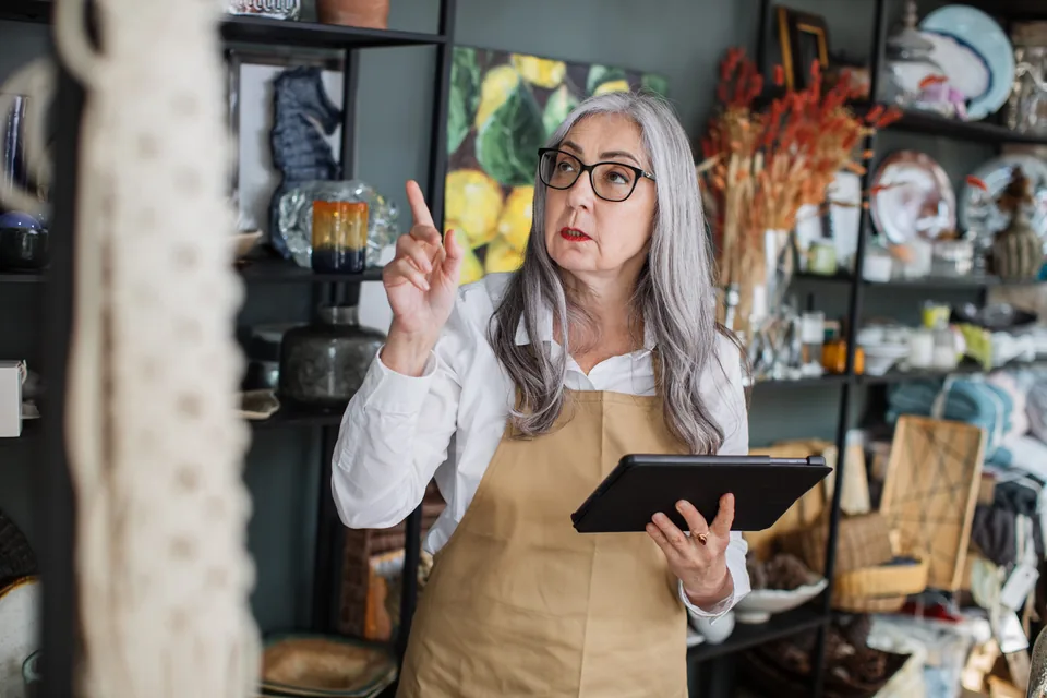 A shopkeeper using a tablet beside shelves of home decor.