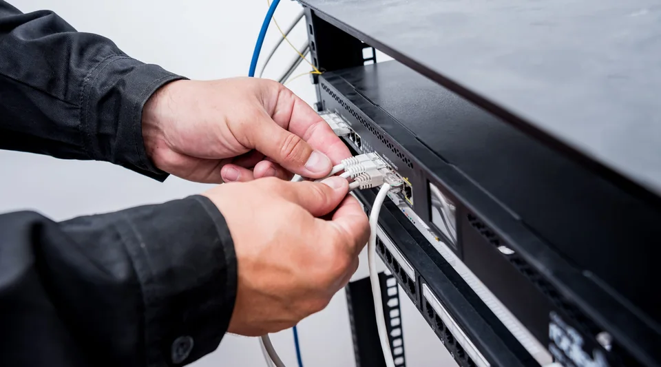 Hands connecting Ethernet cables to a network switch in a rack.